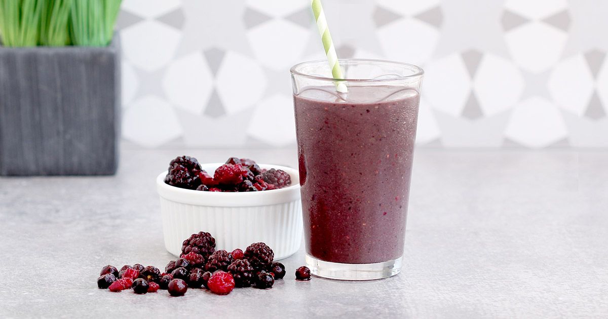 Berry smoothie beside a bowl of frozen berries